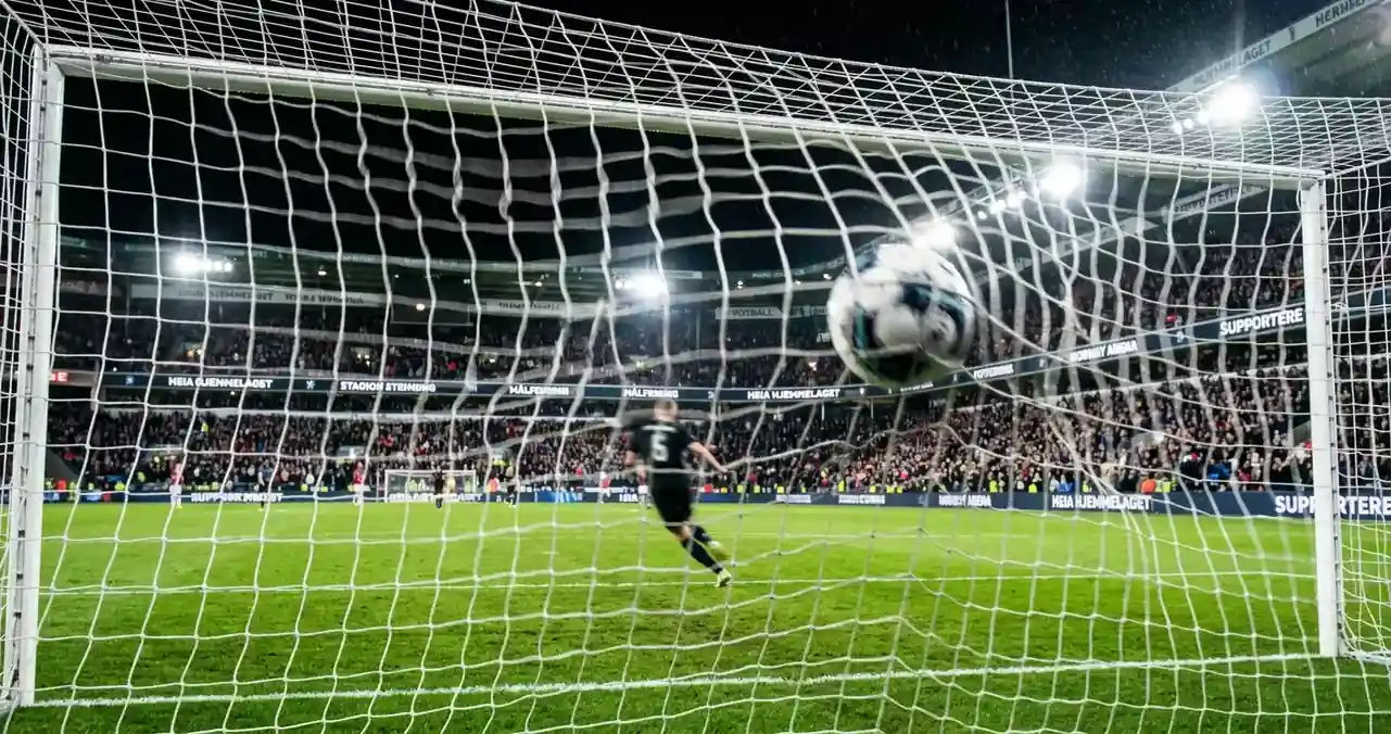 Et fotballmål sett bakfra med ballen i nettet under en opplyst kveldskamp